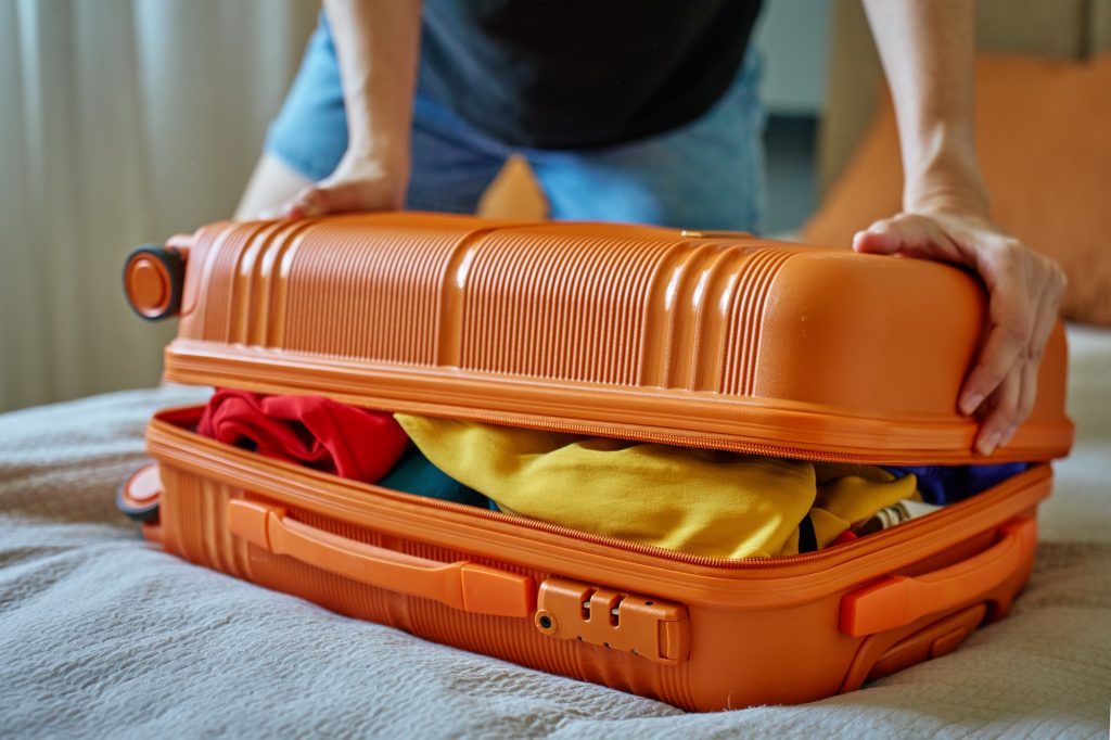Woman closing suitcase full with clothes, preparing for travel